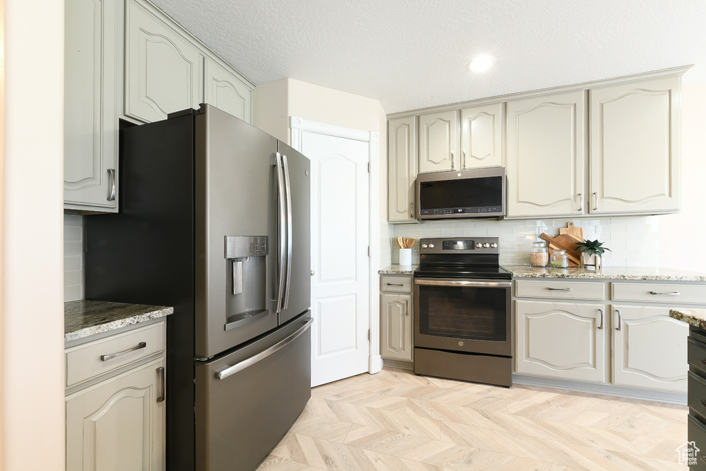 Kitchen with light stone counters, appliances with stainless steel finishes, backsplash, and light parquet flooring