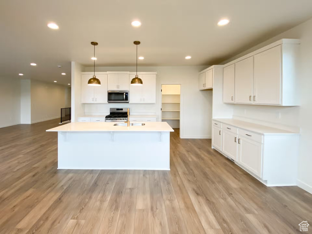 Kitchen featuring a kitchen island with sink, gas range, white cabinets, hanging light fixtures, and light hardwood / wood-style floors