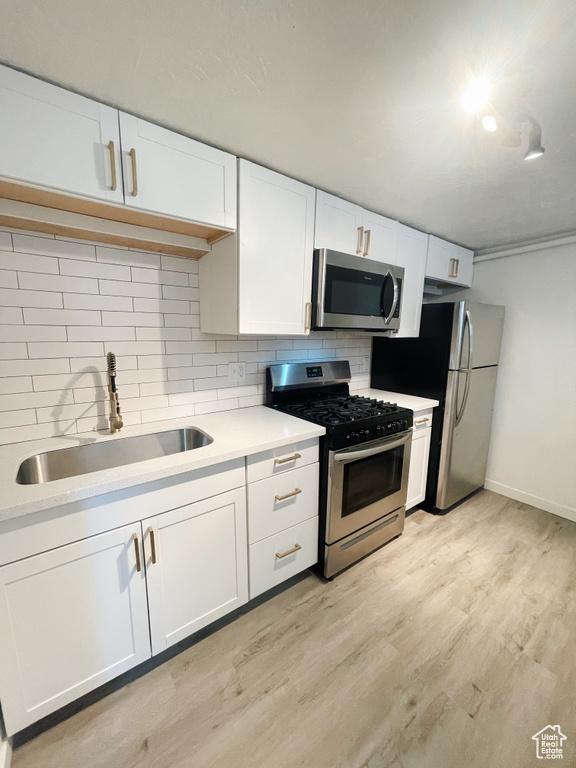 Kitchen with backsplash, stainless steel appliances, light hardwood / wood-style floors, white cabinetry, and sink