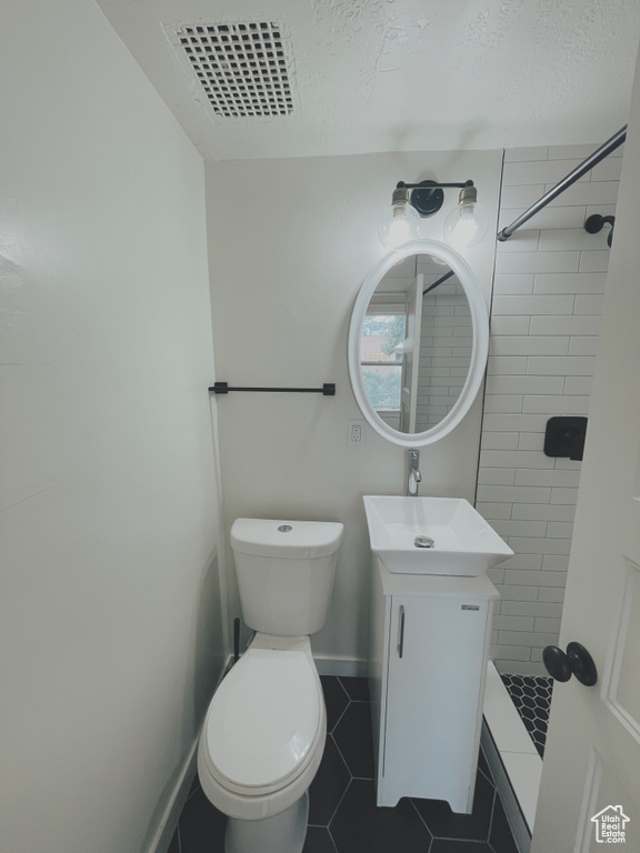 Bathroom featuring tiled shower, toilet, tile flooring, and vanity