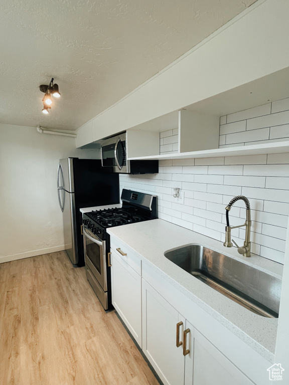 Kitchen with stainless steel appliances, light hardwood / wood-style floors, tasteful backsplash, white cabinets, and sink