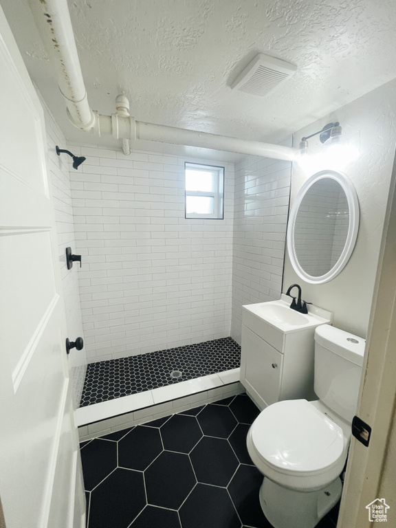 Bathroom with a tile shower, toilet, tile flooring, a textured ceiling, and vanity