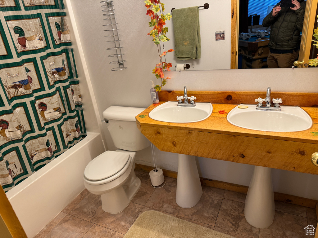 Bathroom with shower / bath combo with shower curtain, dual sinks, toilet, and tile flooring