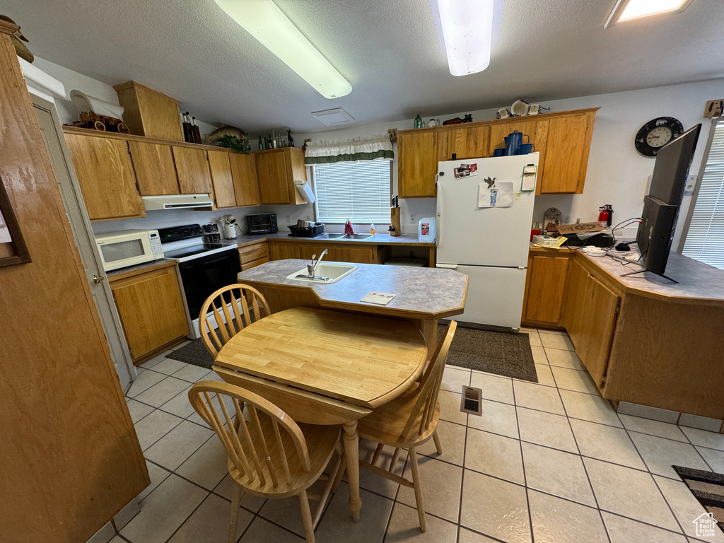 Kitchen featuring white appliances, sink, light tile floors, a textured ceiling, and an island with sink