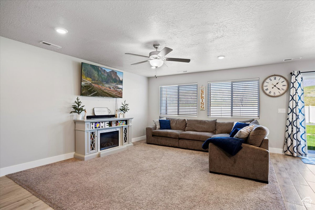 Living room with ceiling fan, a textured ceiling, and light wood-type flooring