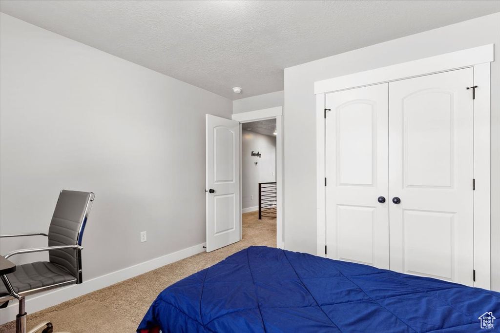 Bedroom with light colored carpet, a textured ceiling, and a closet