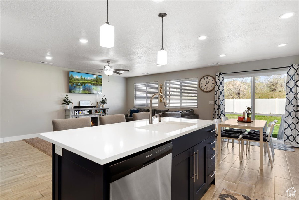 Kitchen featuring hanging light fixtures, ceiling fan, dishwasher, an island with sink, and sink
