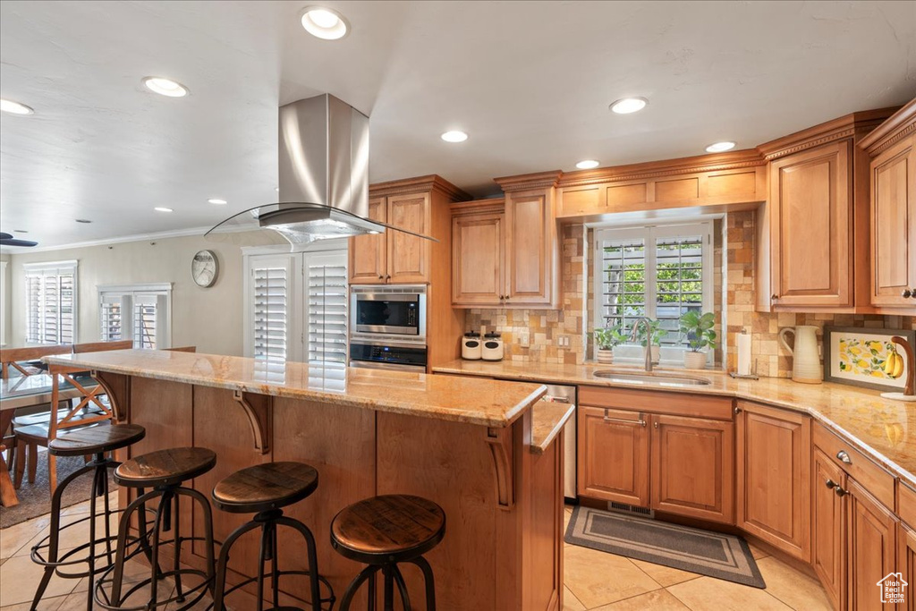 Kitchen featuring island range hood, appliances with stainless steel finishes, sink, light tile floors, and tasteful backsplash
