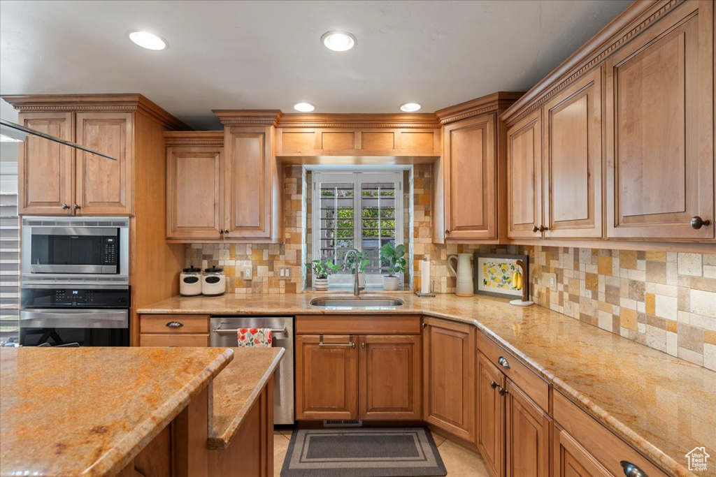 Kitchen featuring appliances with stainless steel finishes, light tile floors, sink, backsplash, and light stone countertops