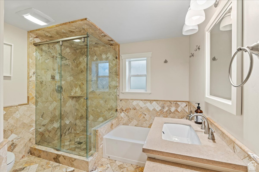 Full bathroom with tile walls, vanity, shower with separate bathtub, tile flooring, and toilet