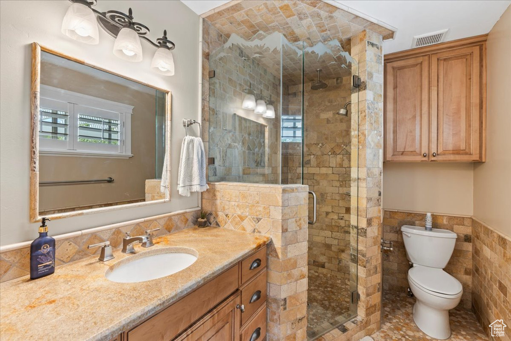 Bathroom with tile walls, an enclosed shower, toilet, and vanity
