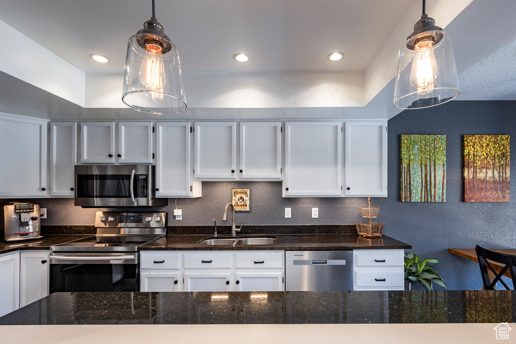 Kitchen featuring hanging light fixtures, white cabinets, appliances with stainless steel finishes, sink, and dark stone countertops