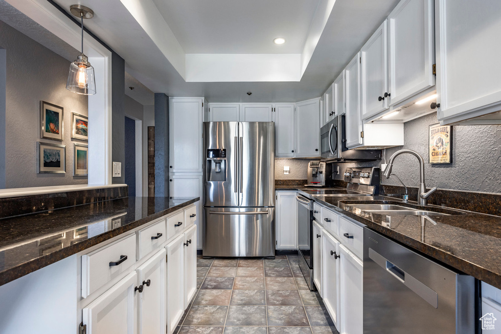 Kitchen featuring hanging light fixtures, white cabinets, stainless steel appliances, light tile floors, and a raised ceiling