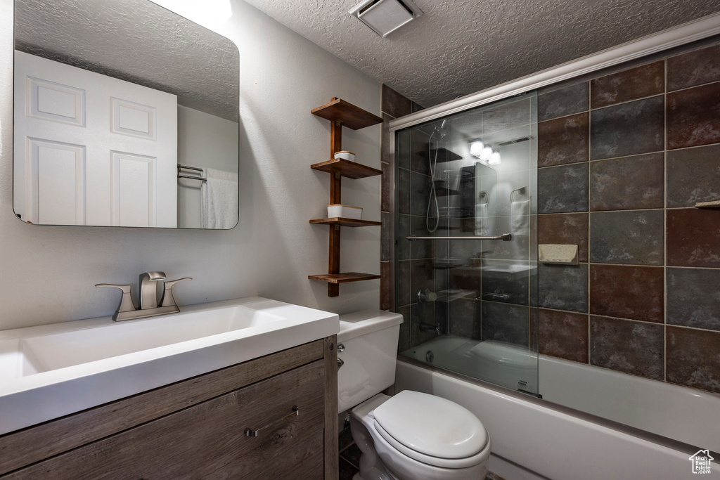 Full bathroom featuring a textured ceiling, vanity, toilet, and bath / shower combo with glass door