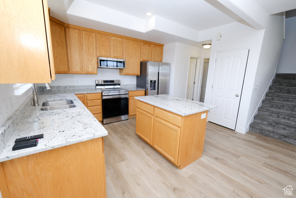 Kitchen featuring light stone countertops, appliances with stainless steel finishes, light hardwood / wood-style flooring, sink, and a center island