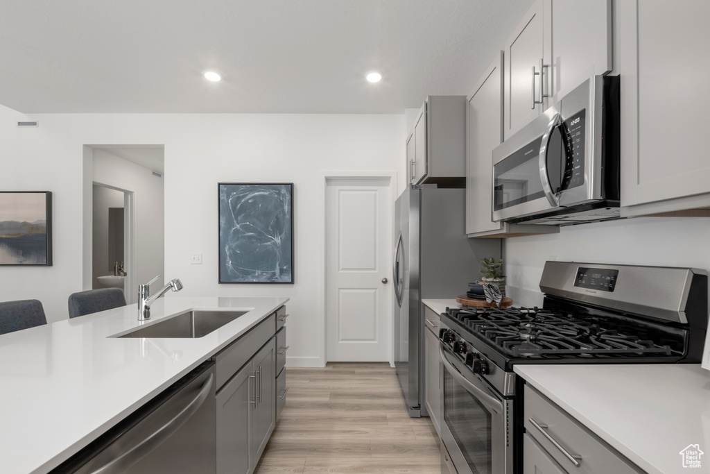 Kitchen with gray cabinetry, appliances with stainless steel finishes, sink, and light wood-type flooring