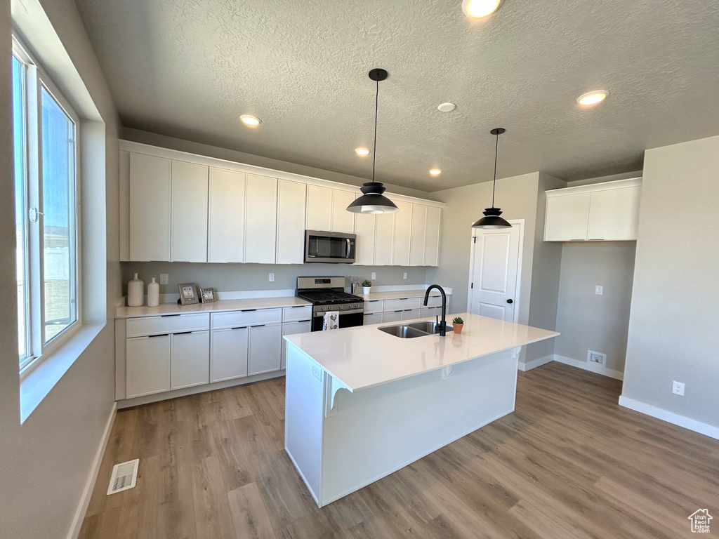 Kitchen featuring hanging light fixtures, white cabinetry, appliances with stainless steel finishes, a center island with sink, and light hardwood / wood-style floors