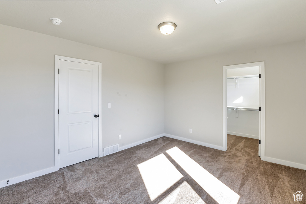 Unfurnished bedroom featuring a spacious closet, a closet, and carpet floors