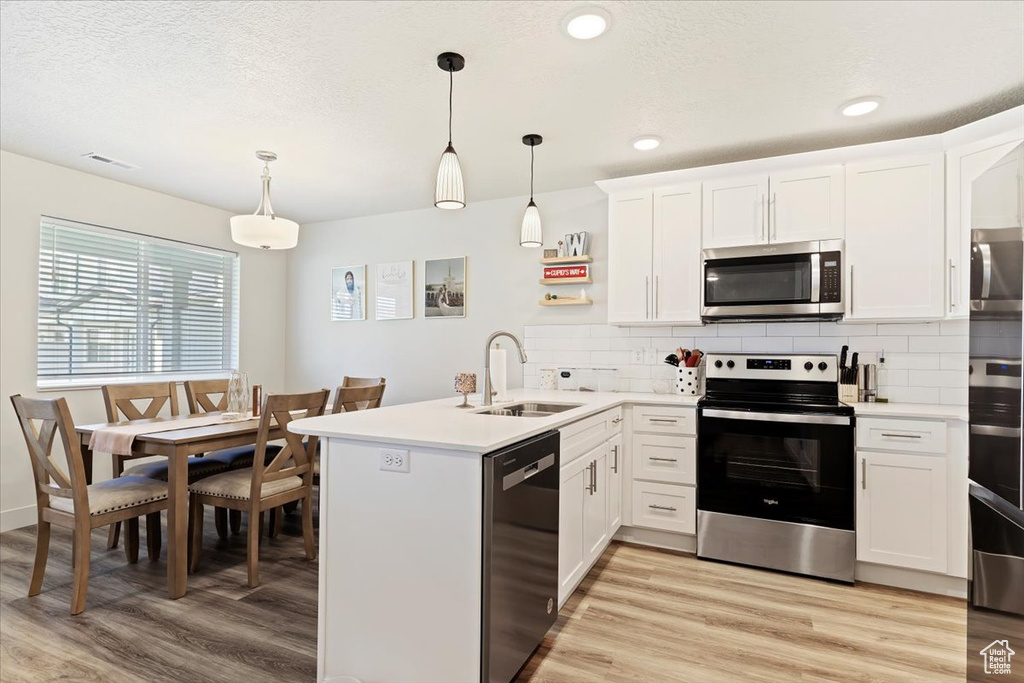 Kitchen with hanging light fixtures, light hardwood / wood-style flooring, kitchen peninsula, appliances with stainless steel finishes, and sink