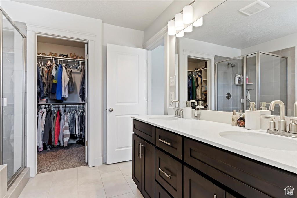 Bathroom with walk in shower, vanity with extensive cabinet space, tile flooring, a textured ceiling, and dual sinks