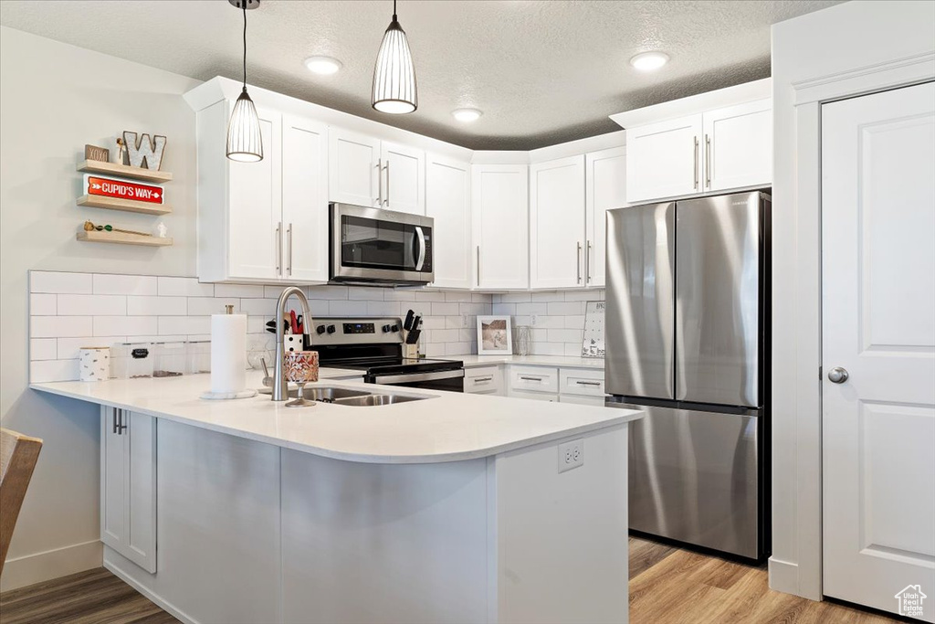 Kitchen with appliances with stainless steel finishes, white cabinets, hanging light fixtures, light hardwood / wood-style flooring, and kitchen peninsula