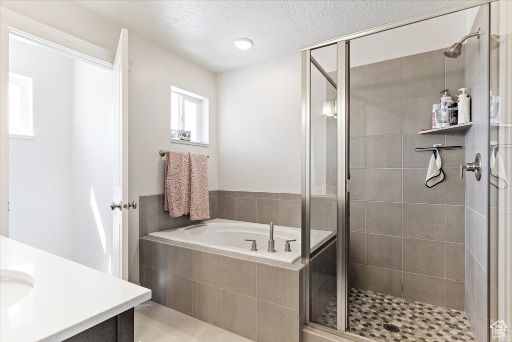 Bathroom featuring a textured ceiling, independent shower and bath, tile floors, and vanity