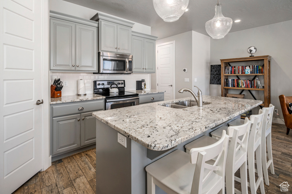 Kitchen featuring decorative light fixtures, gray cabinetry, dark hardwood / wood-style floors, appliances with stainless steel finishes, and an island with sink
