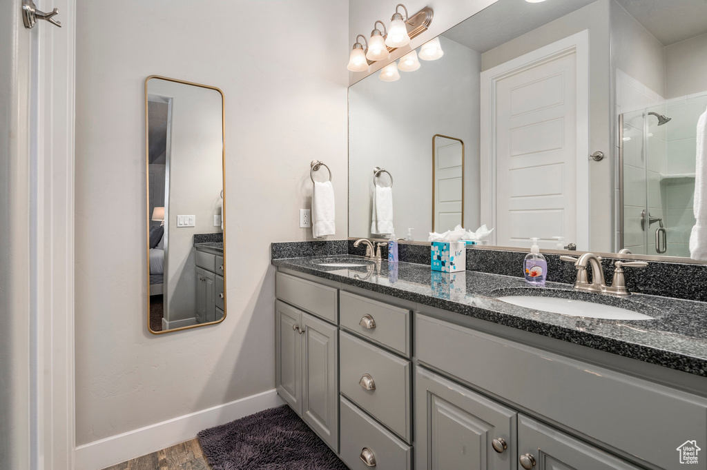 Bathroom featuring large vanity, a shower with shower door, hardwood / wood-style flooring, and dual sinks