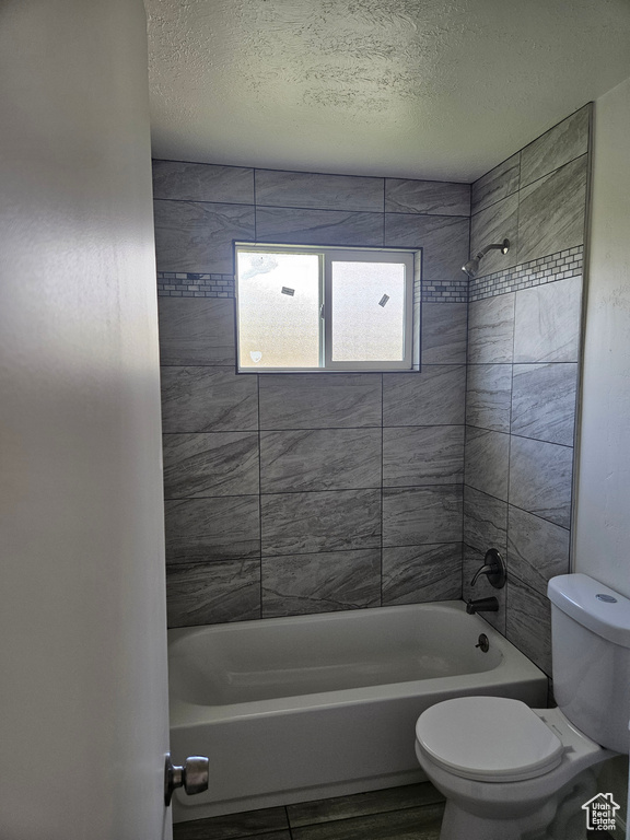 Bathroom with tiled shower / bath combo, a textured ceiling, and toilet