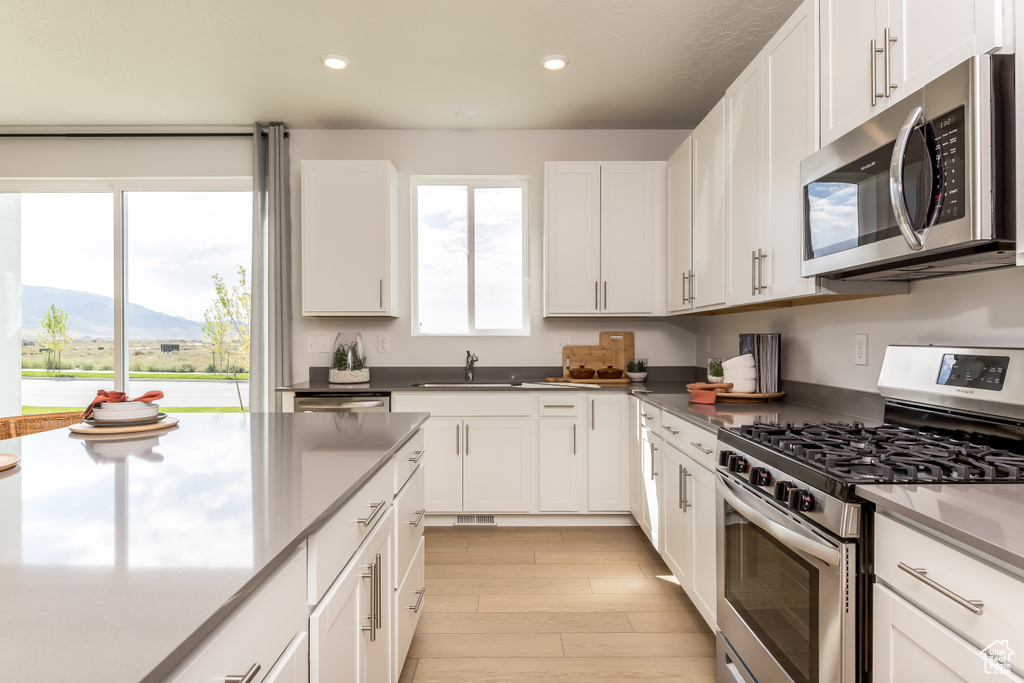Kitchen featuring appliances with stainless steel finishes, a mountain view, sink, light wood-type flooring, and white cabinetry