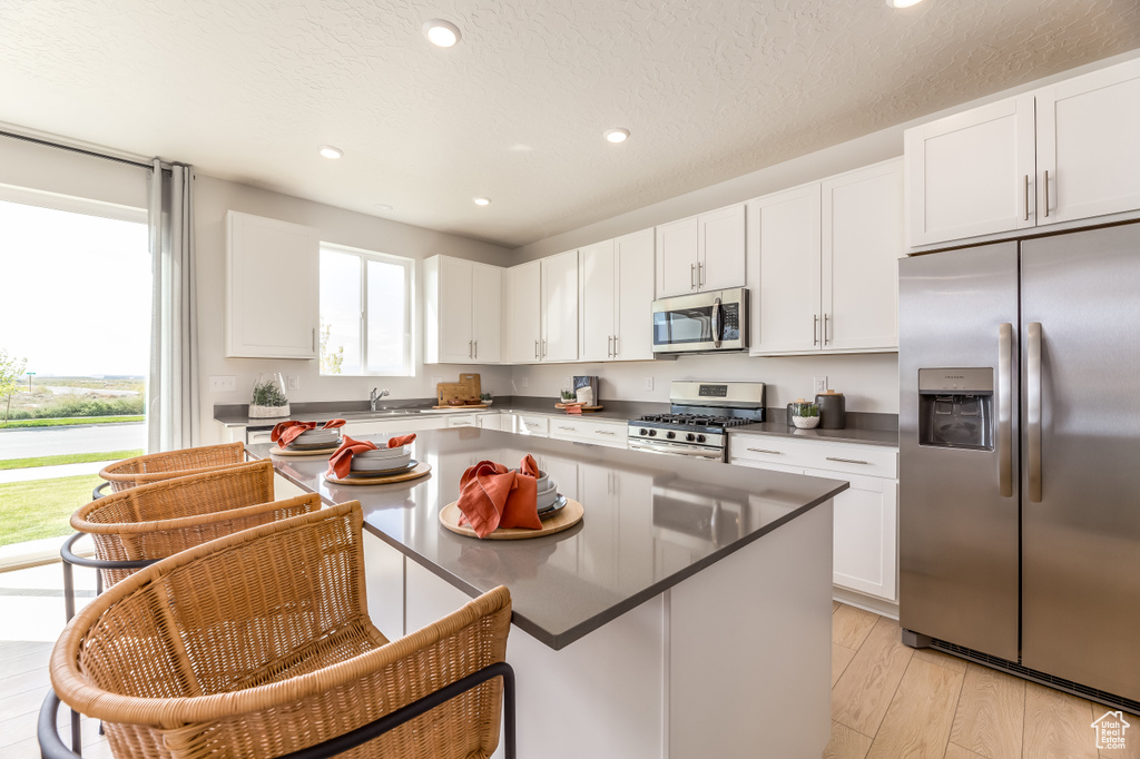Kitchen with white cabinets, light hardwood / wood-style floors, appliances with stainless steel finishes, and plenty of natural light