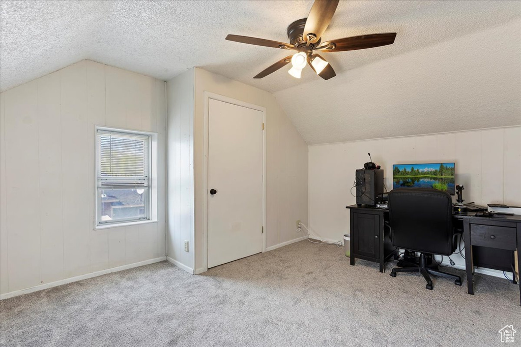 Home office featuring light colored carpet, vaulted ceiling, ceiling fan, and a textured ceiling