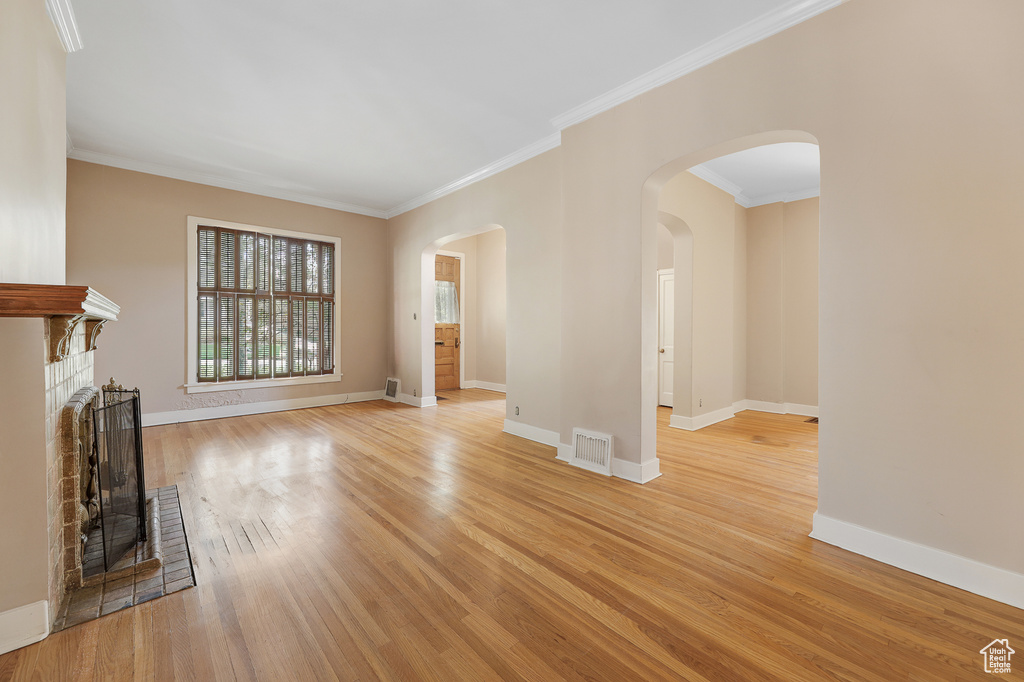 Unfurnished living room with ornamental molding, a brick fireplace, and light wood-type flooring