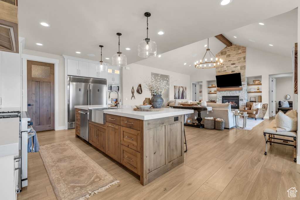 Kitchen with white cabinets, pendant lighting, a center island with sink, and light hardwood / wood-style floors