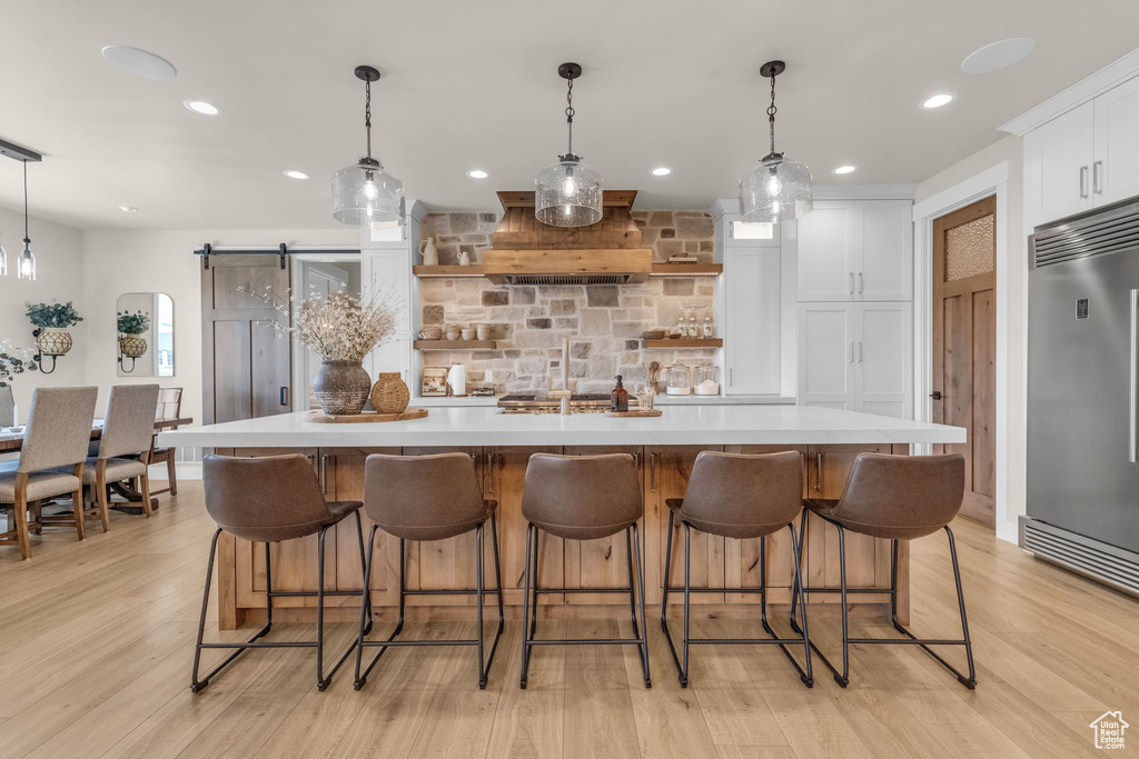 Kitchen with backsplash, white cabinetry, built in fridge, light hardwood / wood-style flooring, and a large island