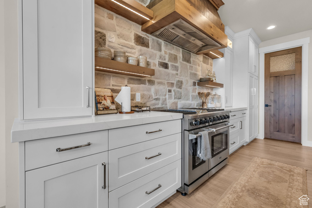 Kitchen with backsplash, double oven range, premium range hood, and white cabinetry