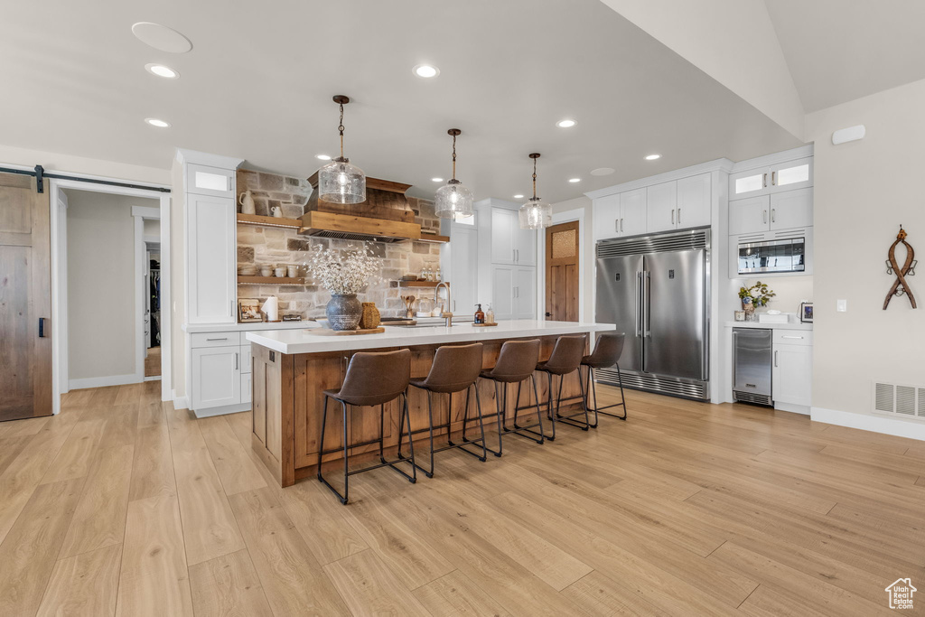 Kitchen featuring a barn door, light hardwood / wood-style floors, backsplash, a kitchen island with sink, and built in appliances