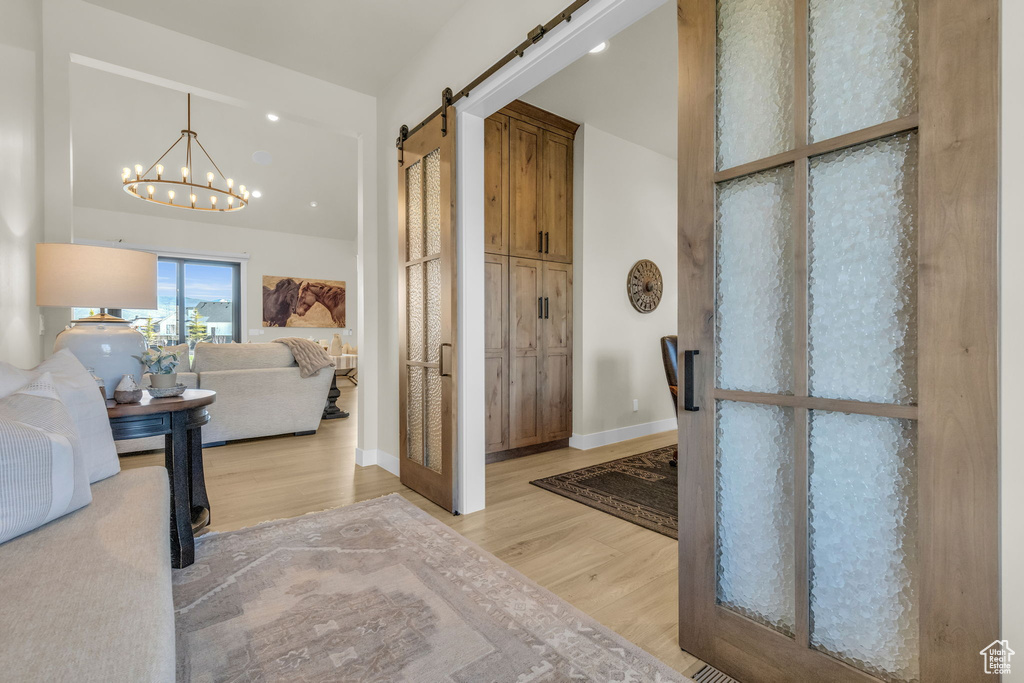 Foyer entrance with light hardwood / wood-style flooring, a notable chandelier, and a barn door