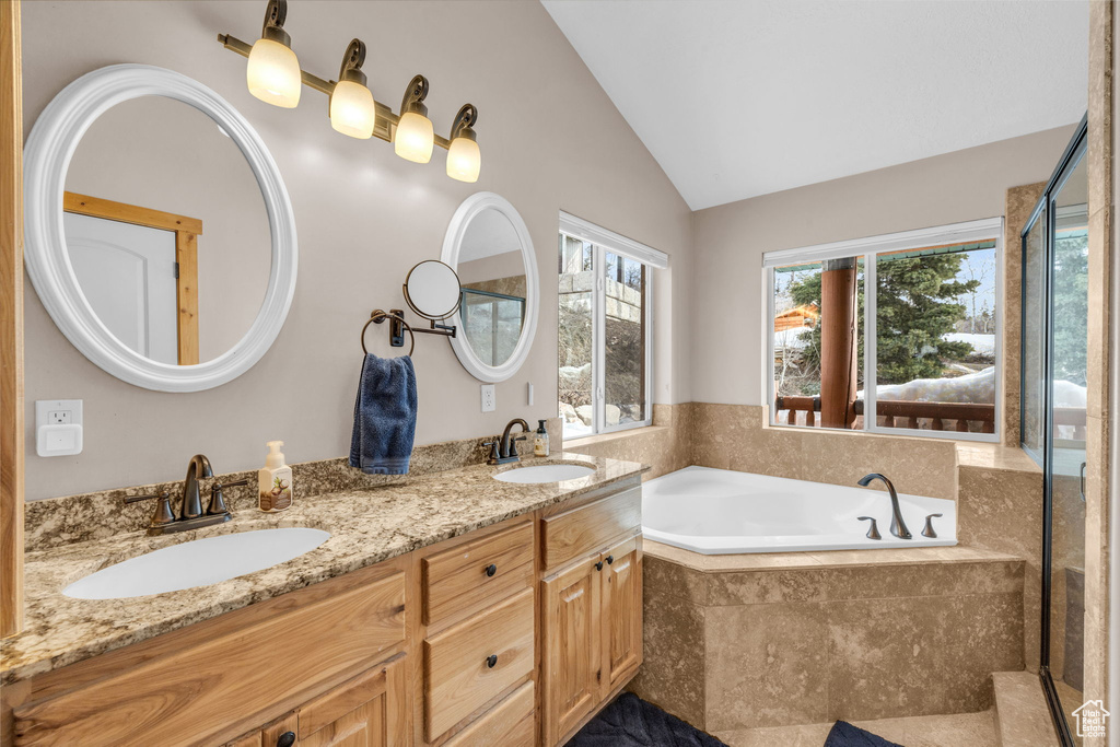 Bathroom featuring vaulted ceiling, a relaxing tiled bath, double sink, and large vanity