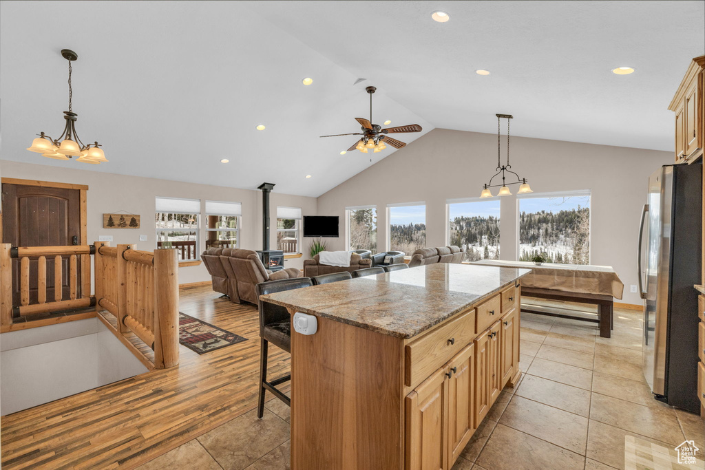 Kitchen featuring a kitchen island, ceiling fan with notable chandelier, light tile flooring, hanging light fixtures, and stainless steel fridge