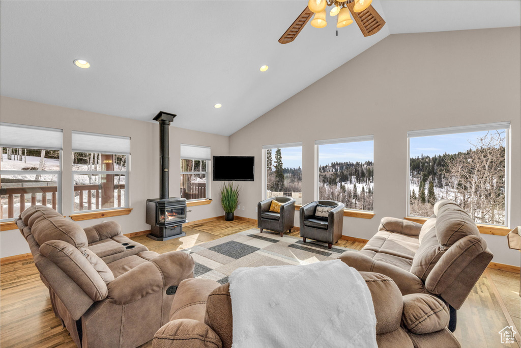 Living room featuring high vaulted ceiling, a wood stove, light hardwood / wood-style flooring, and ceiling fan