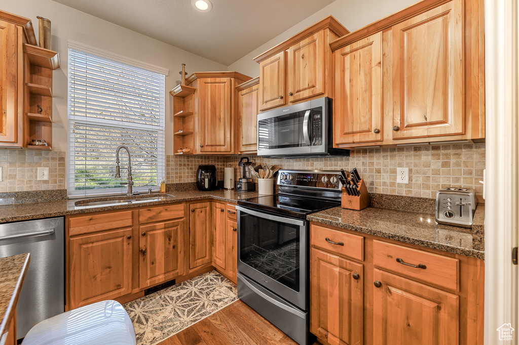 Kitchen with backsplash, light hardwood / wood-style flooring, stainless steel appliances, dark stone counters, and sink