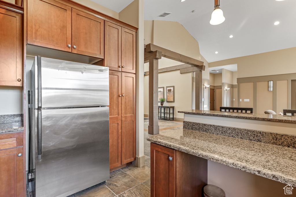 Kitchen with light stone counters, decorative light fixtures, stainless steel fridge, tile floors, and vaulted ceiling