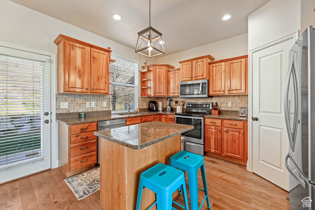 Kitchen with backsplash, light hardwood / wood-style floors, stainless steel appliances, and a kitchen island