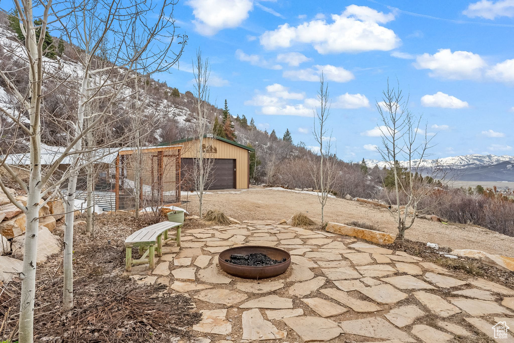 View of patio featuring a garage, a mountain view, an outdoor fire pit, and an outdoor structure