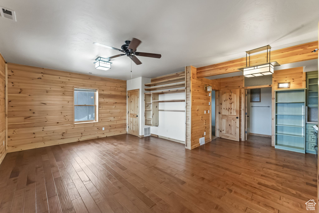 Empty room featuring wood-type flooring, ceiling fan, and wooden walls