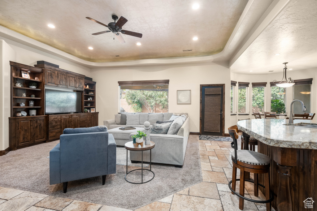 Carpeted living room featuring ceiling fan, sink, and a tray ceiling