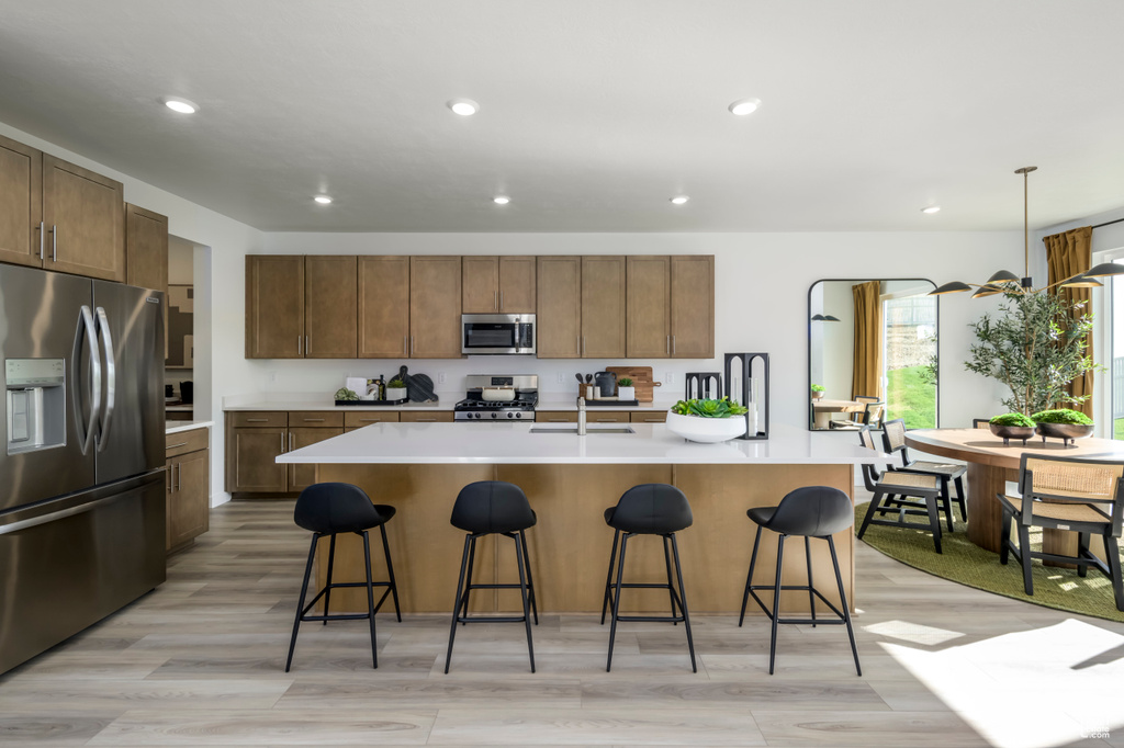 Kitchen with appliances with stainless steel finishes, light hardwood / wood-style flooring, a breakfast bar area, an island with sink, and pendant lighting