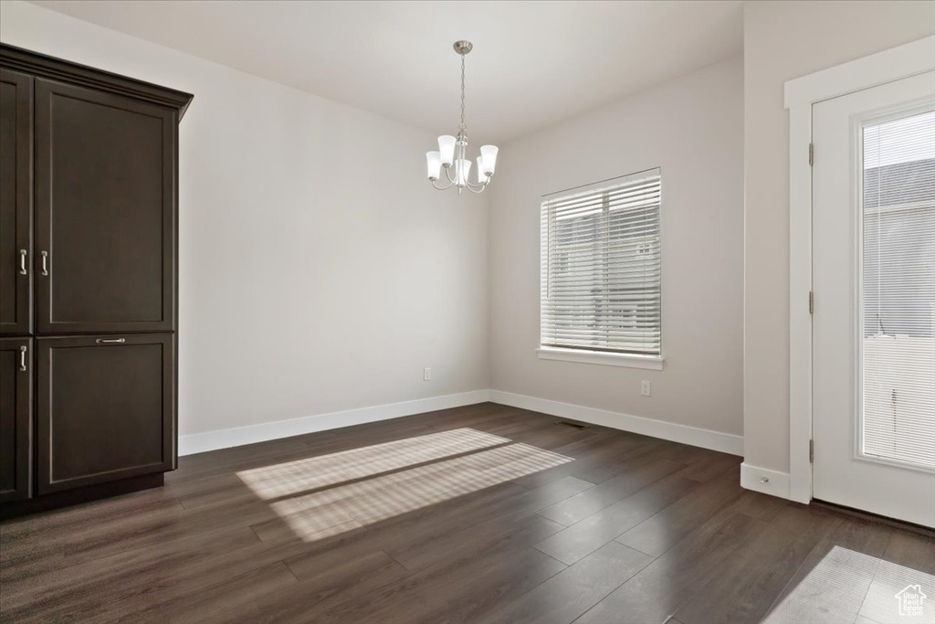 Empty room with dark hardwood / wood-style flooring and a chandelier