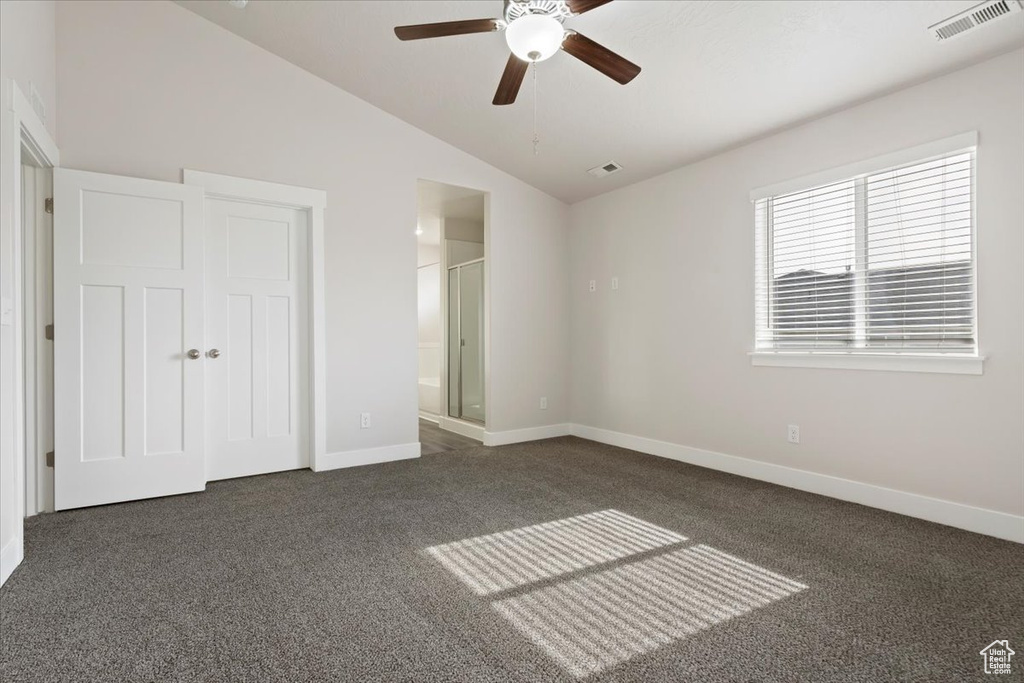Unfurnished bedroom featuring dark carpet, a closet, ensuite bathroom, ceiling fan, and lofted ceiling